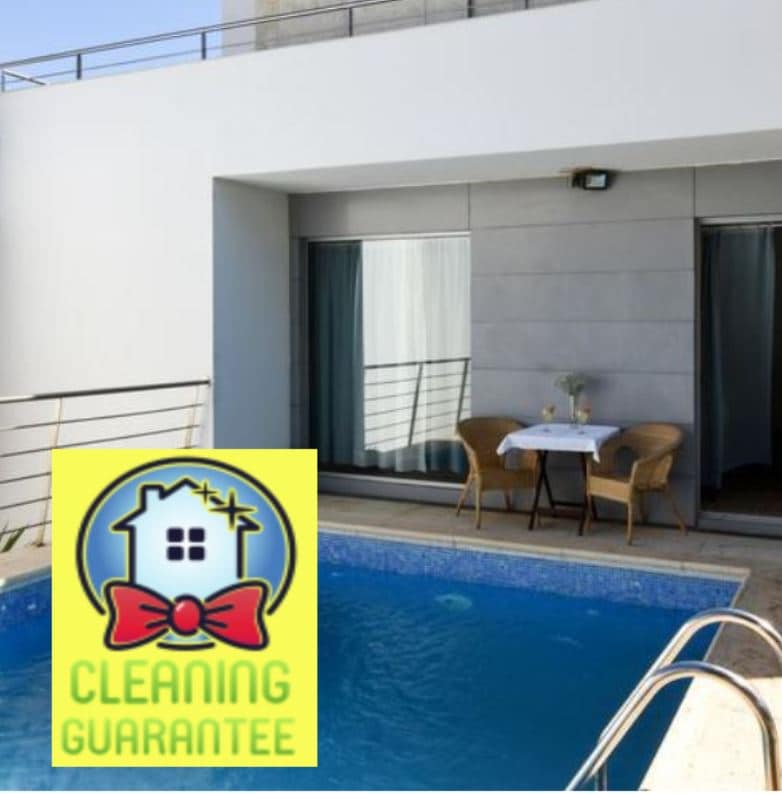 A small outdoor seating area is positioned beside a private pool, featuring two comfortable chairs and a table. Large windows reflect a modern, minimalistic design. The patio area allows for easy access to the pool, enhancing relaxation opportunities.