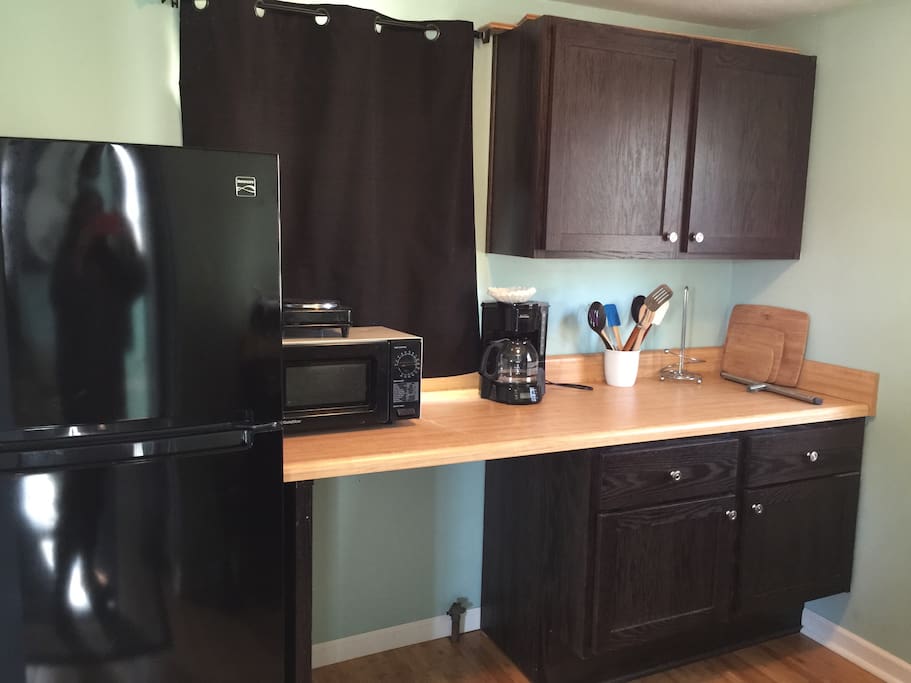 Part of kitchen area which includes refrigerator, counter space, microwave, coffee maker, hotplate.