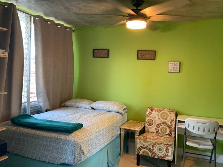 Green guest room with full size bed, desk, and printer.