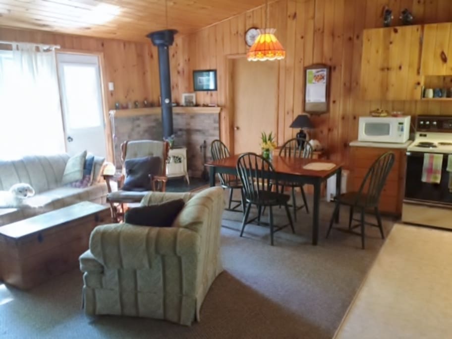 Sunny interior showing large picture window, living/dining area and and wood stove.