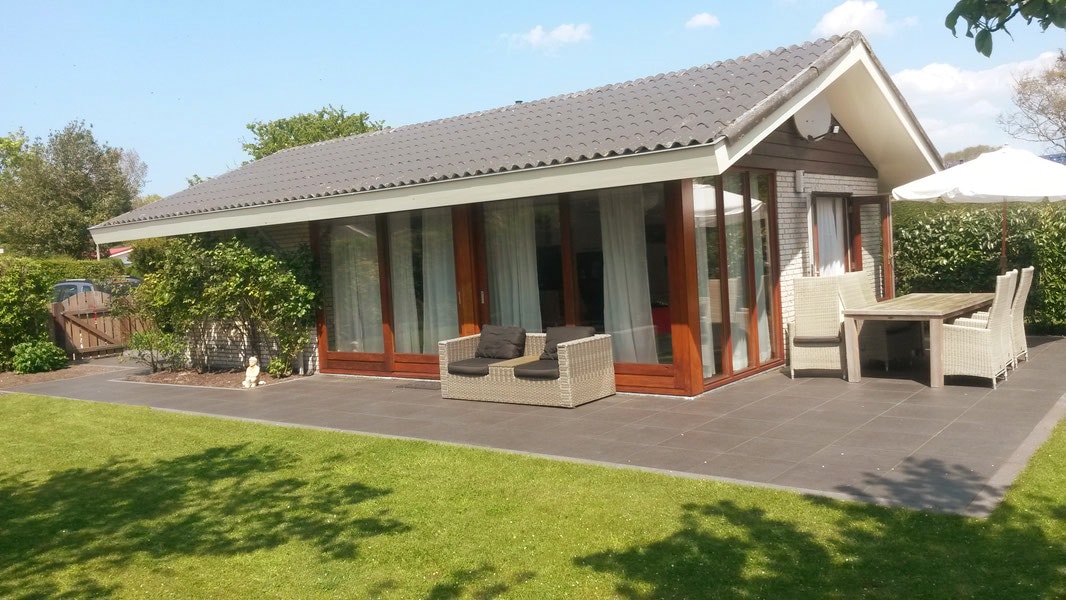 The bungalow features a spacious patio area with comfortable outdoor seating and a dining table. Large windows allow natural light to fill the interior, while well-maintained greenery surrounds the property, creating a serene outdoor space for relaxation.