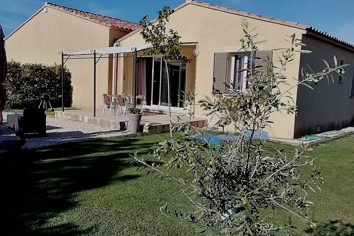 The exterior of the house features a spacious terrace with a canopy, adjacent to a well-maintained garden. Seating arrangements include a small dining table and chairs, while a decorative plant adds a touch of greenery to the scene. The yellow walls reflect abundant natural light.