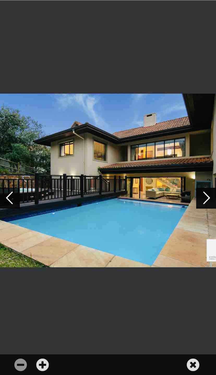 An outdoor private swimming pool is featured, surrounded by a stone patio and a wooden railing. The two-story house in the background is complemented by large windows reflecting the evening sky, which enhances the tranquil setting.