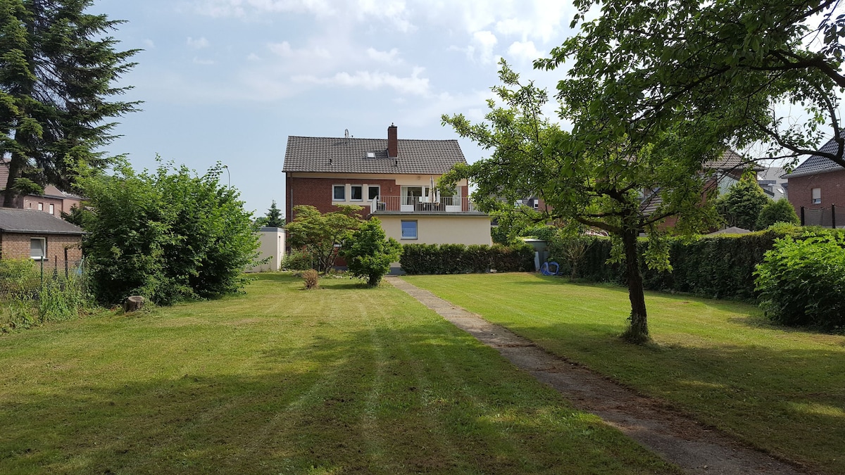 A spacious garden area is visible, featuring well-maintained grass and a clear pathway leading to a two-story building. Lush green trees and shrubs line the perimeter, providing a sense of openness and tranquility.