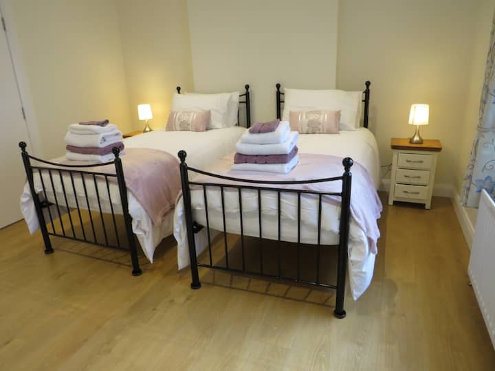 Habitación doble, baño privado, abajo. Estas camas se pueden combinar para hacer una cama doble grande con sábana bajera y edredón súper king. Tiene armario, cómoda con espejo de tocador,  televisor de 32pulgadas y espejo de cuerpo entero en la pared.