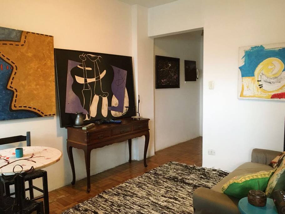 Sala de estar confortável com sofá cama, mesa, aparador e muita arte para encantar e agradar os olhos e o coração.