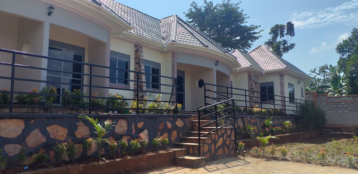 A well-maintained exterior view of a single-story home is presented, featuring a welcoming entry with a rounded doorway. Surrounding gardens with colorful flowers and carefully arranged stone pathways enhance the property. The pitched roof and stylish windows add architectural interest.