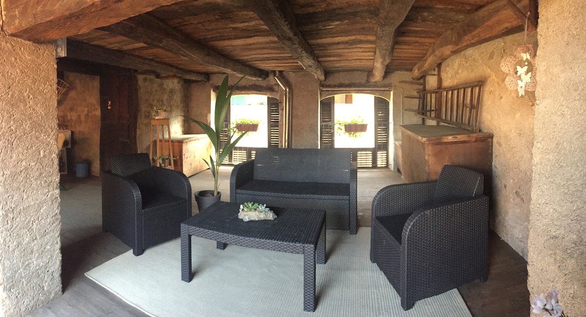A cozy seating area is presented with dark wicker furniture, including two armchairs and a sofa, arranged around a small table. A light-colored rug enhances the warm wooden flooring. Natural light streams in from windows, providing a relaxed atmosphere for gatherings.