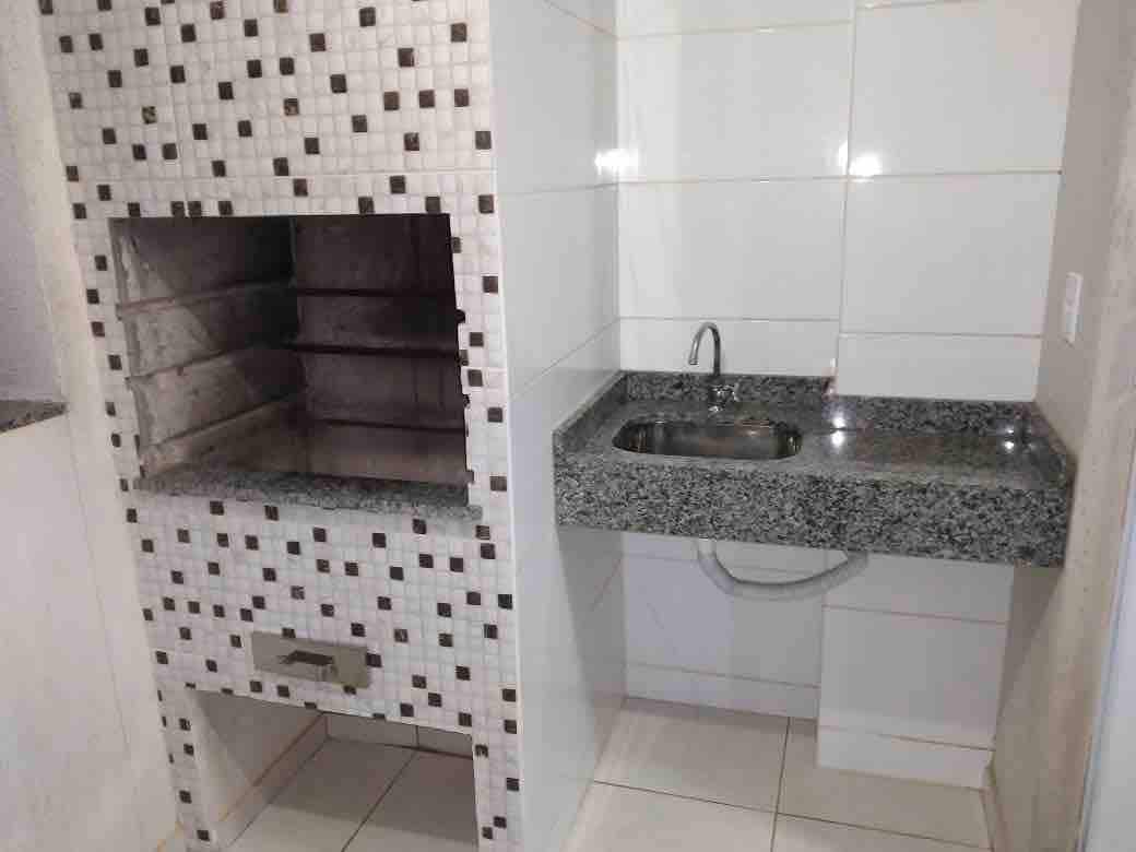 A modern kitchen area is showcased, featuring a built-in grill made of stone tiles and a countertop with a sink. The surfaces are finished in glossy white tiles, and the geometric pattern adds subtle visual interest.