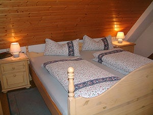 A cozy bedroom features a wooden ceiling and soft lighting from bedside lamps. The spacious bed is adorned with floral-patterned bedding and decorative pillows. A nightstand holds a small clock, while a gentle area rug completes the inviting atmosphere.