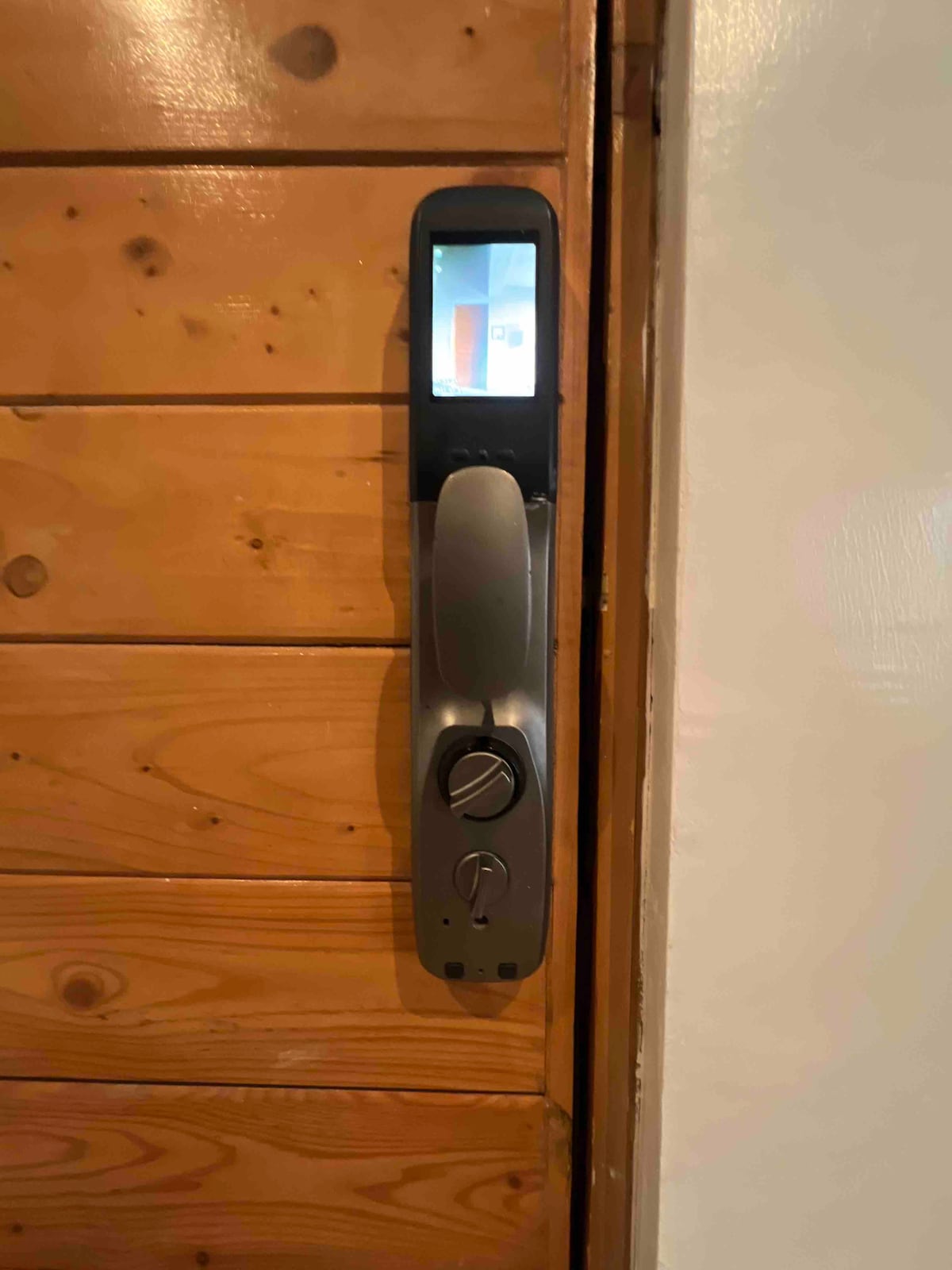 A modern keyless entry system is mounted on a wooden door. The sleek design features a digital screen and two control knobs, presenting a secure and convenient access point to the apartment.