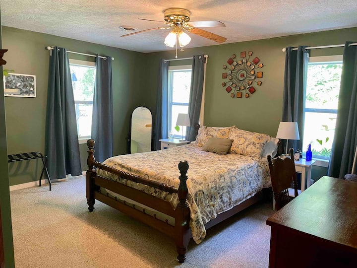 The master bedroom has a queen size bed with a memory foam mattress pad, a large desk, a dresser, a place to hang clothes, and large windows with blackout curtins. 