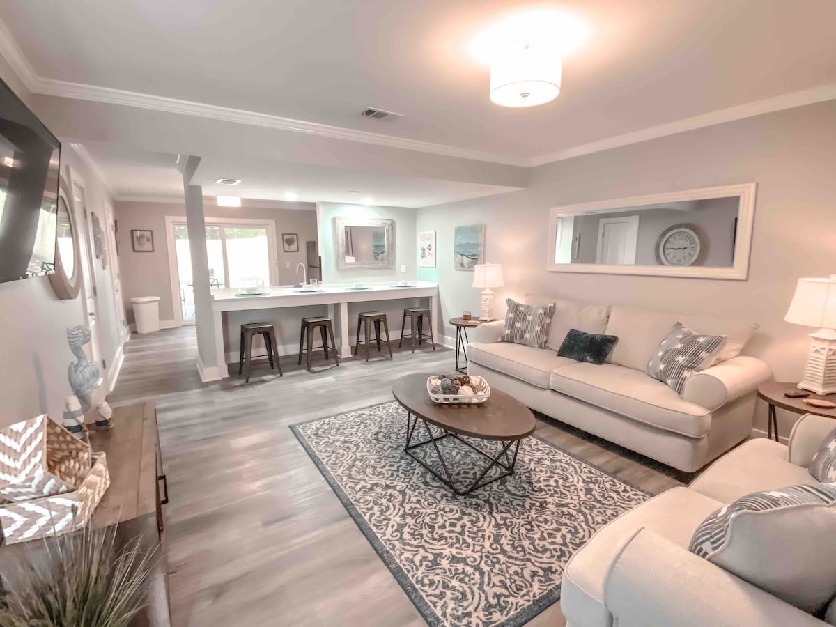 A spacious living room is presented with comfortable seating arranged around a central coffee table. A large area rug enhances the space, while natural light filters through the sliding glass doors, leading to the outdoor patio. A flat-screen TV and tasteful decor complete the inviting environment.
