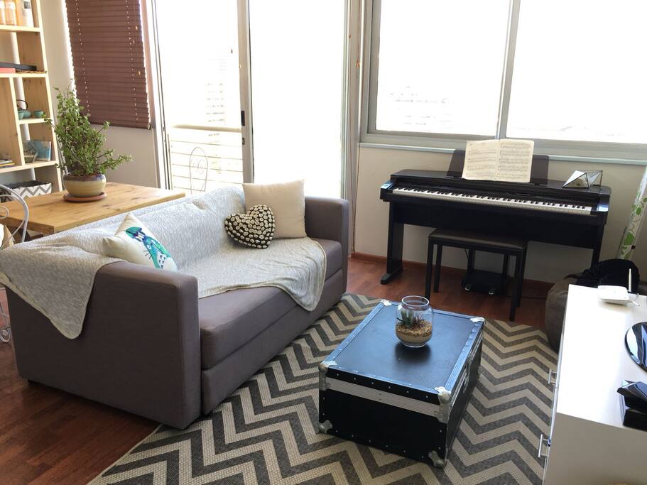The living room has a TV, sleeper couch and piano.