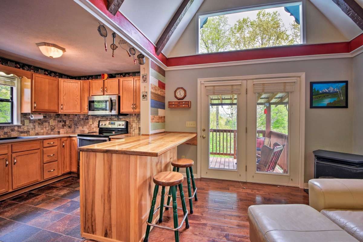 A spacious kitchen features natural wood cabinetry and an island with seating for two. Large windows allow ample natural light, illuminating the space. The adjoining area opens to a deck, enhancing the seamless indoor-outdoor connection.