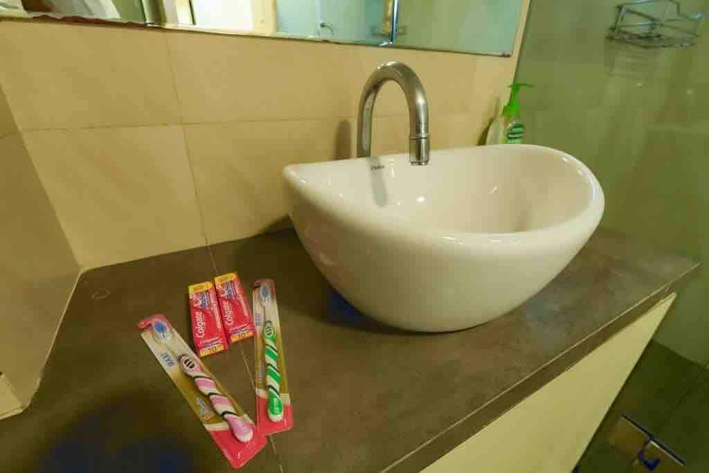 A stylish washbasin with a modern faucet is positioned on a sleek countertop. Two toothbrushes are placed on the surface beside a colorful tube of toothpaste. A minimalist aesthetic is evident in the simple, clean lines of the bathroom.