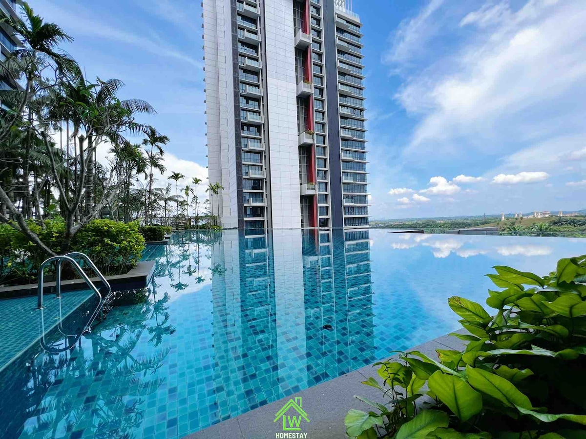 An expansive infinity pool is observed, reflecting the modern building alongside lush greenery. The tranquil water surface mirrors the sky and surrounding landscape, creating a serene outdoor space for relaxation.