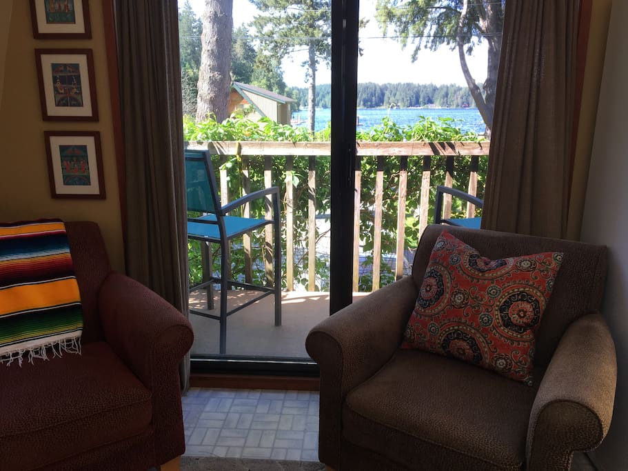 Living area cozy chairs in front of sliding glass doors that open onto balcony where you can sit on stools looking out towards lake.