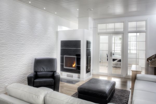 An inviting living area features a sleek black fireplace surrounded by light-colored furniture. A comfortable armchair is positioned adjacent to a soft ottoman, while large glass doors allow ample natural light and offer a view of the dining area beyond.