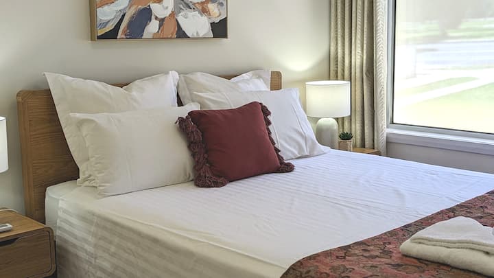 تحتوي غرفة النوم رقم2 على سرير بمقاس كوين جديد بمرتبة فاخرة ونقاط طاقة بجانب السرير ومصابيح. تحتوي الغرفة على مكيف هواء بنظام سبليت ومروحة سقف. يمكن للضيوف تجربة شمس الصباح من خلال فتح الستائر.