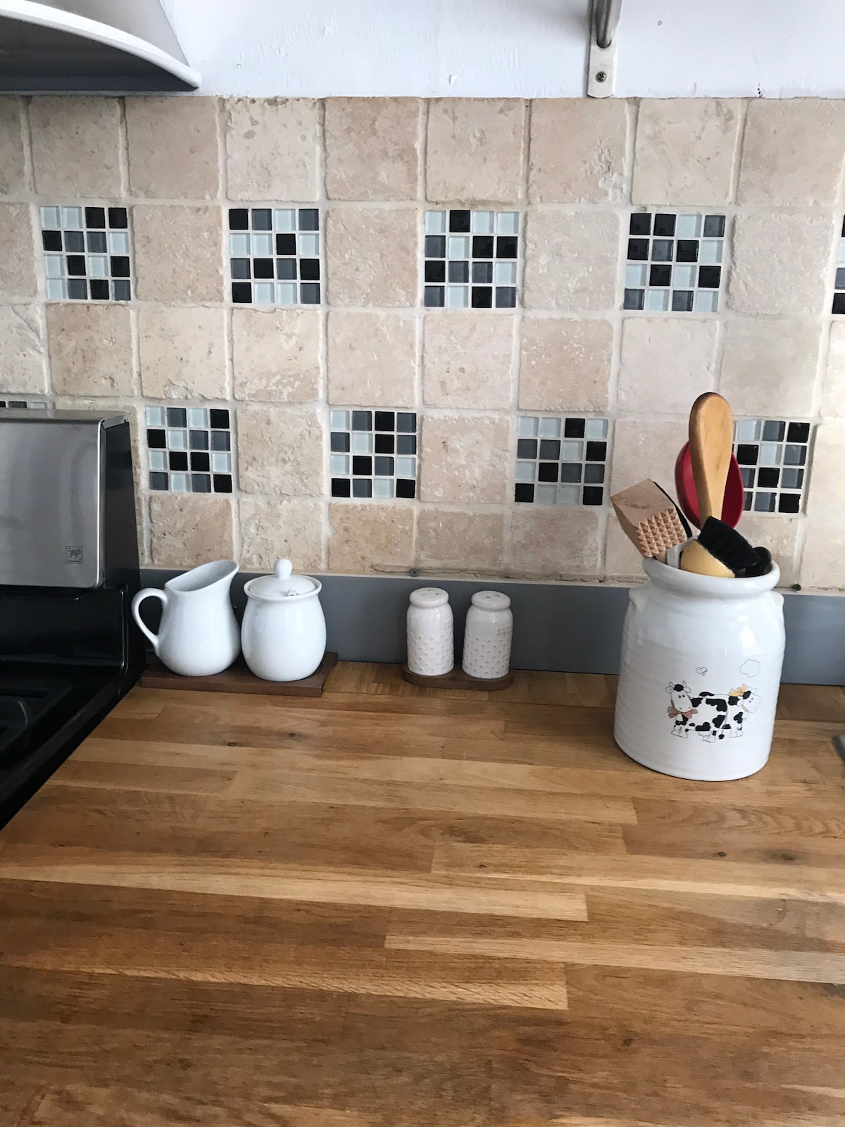The kitchen counter features a wooden surface with a small selection of ceramic containers. A white jug and two small speckled jars are placed next to a decorative canister adorned with a cow motif, which holds kitchen utensils.