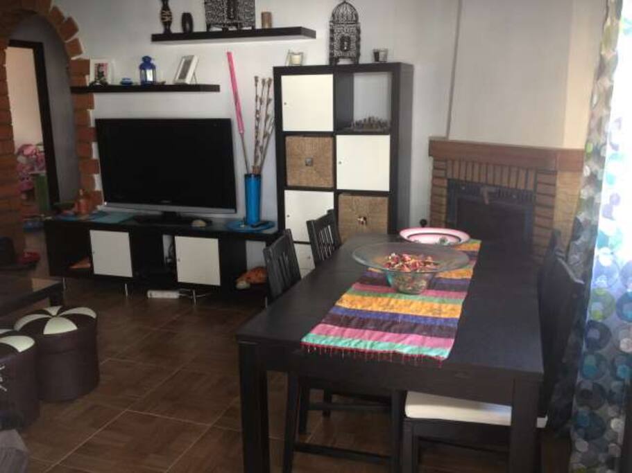 Fabuloso Salón/Comedor con chimenea motorizada que emite calor sin olores tanto al salón como al dormitorio principal. Dispone de mesa con 4 sillas, entarba donde pueden dormir 2 personas comodamente, mesa de té con 4 puff, televisor con TDT (canales de Marruecos y España) y acceso a terraza de 9m2 con mesa de 6 sillas y barbacoa.