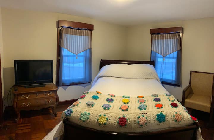 تحتوي غرفة النوم الثانية على سرير بمقاس كبير مع تلفزيون Roku بشاشة مسطحة وخزانة وطاولة وحدة تحكم صغيرة وكرسي.