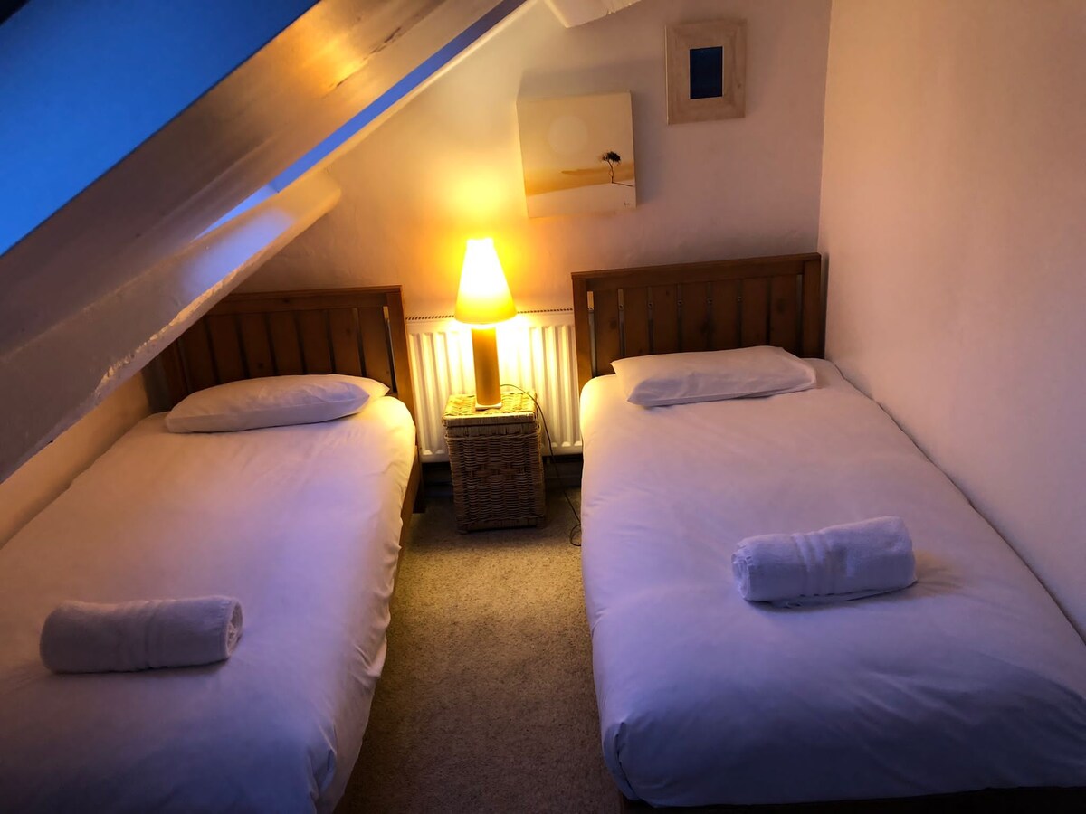 غرفة نوم علوية، مرتبطة بغرفة نوم واحدة أخرى.  أسرّة وأثاث جديد في فبراير 2022.  يرجى ملاحظة أن الدرج المؤدي إلى غرفتي النوم الثانية والثالثة في دور علوي، وهو مناسب فقط للأشخاص الذين يتمتعون بالتنقل الكامل