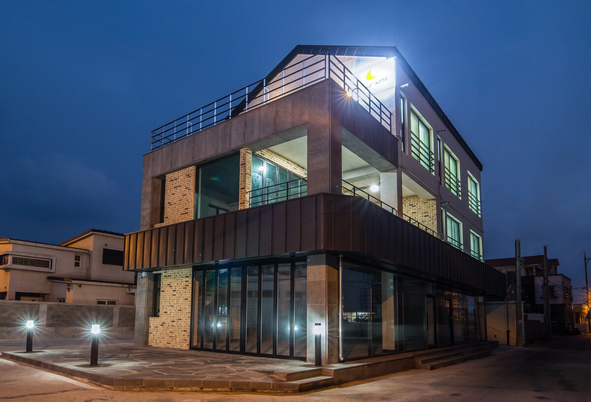 The modern building is highlighted by a sleek facade with large glass windows and an inviting entrance. A well-lit outdoor area features stylish lighting fixtures, providing a warm glow against the night sky.