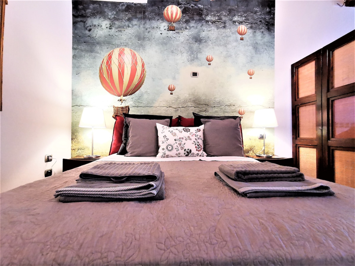 A comfortable sleeping area features a spacious bed adorned with soft linens. Decorative pillows add subtle color, while a mural of hot air balloons provides a unique backdrop. Soft lighting from bedside lamps enhances the tranquil ambiance.