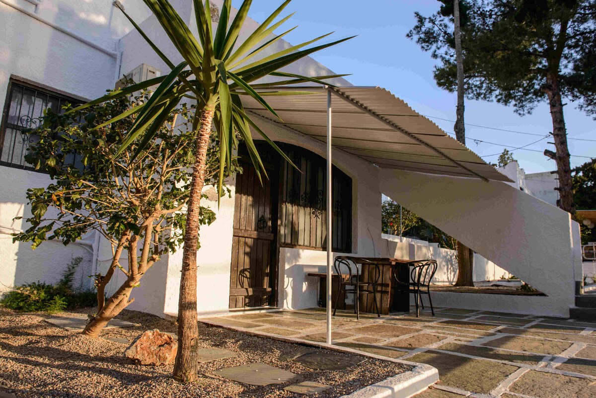 The exterior of the residence showcases a modern design, featuring a covered patio area with a table and chairs. A lush green plant adds a natural touch to the surroundings, while the clean lines of the building create a welcoming entrance.