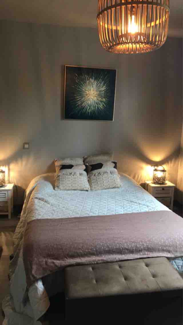 A cozy sleeping area features a spacious bed adorned with decorative pillows and a patterned throw. Soft bedside lamps provide warm lighting, and a piece of wall art adds a focal point. A bench at the foot of the bed offers additional seating.