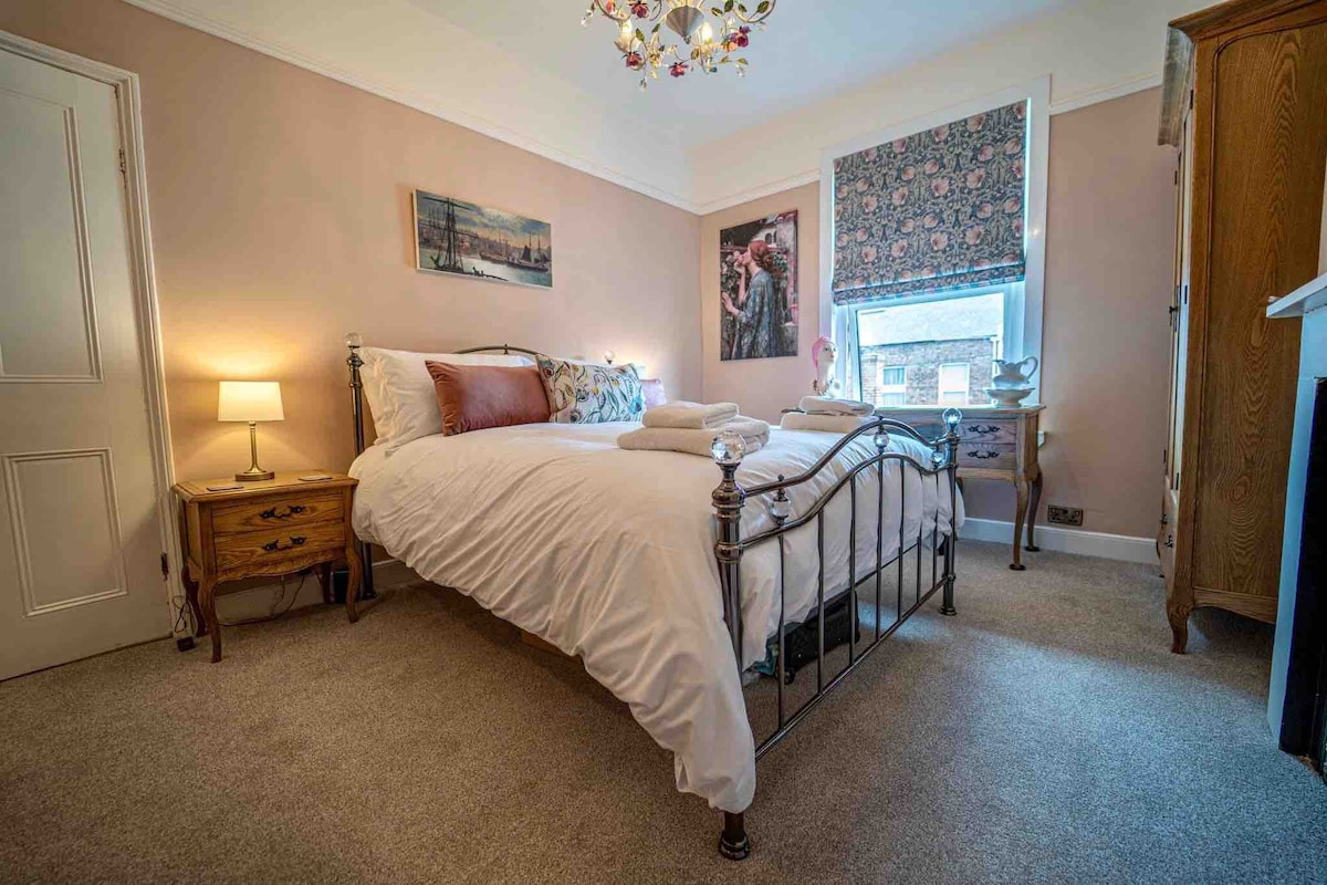 ห้องนอนคิงไซส์สีชมพูสไตล์วิคตอเรียที่สวยงาม ด้วย William Morris Roman blind, Pre-Raphaelite & Grimshaw prints, dressing table, fan, hairdrier, and luggage rest, plus quirky mannequin head & lovely floral chandelier. ทุกอย่างมีคุณภาพดีเยี่ยม 