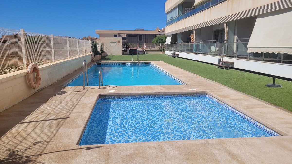 A well-maintained outdoor area features two swimming pools surrounded by neatly landscaped grass. One pool is designed for relaxation, while the other offers a space for swimming. Sun loungers are positioned nearby, creating an inviting atmosphere for outdoor enjoyment.