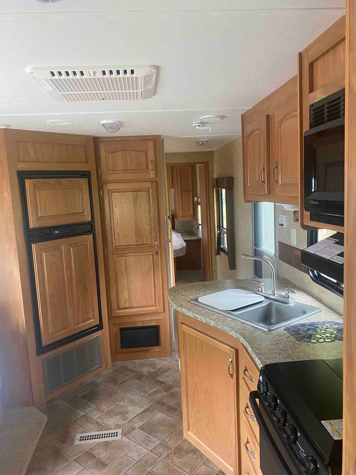 The interior kitchen space features wooden cabinetry and a granite countertop. A sink is incorporated within the countertop. Appliances, including a stove and refrigerator, are visible, along with storage areas. The layout provides easy access to the living area and bedroom.
