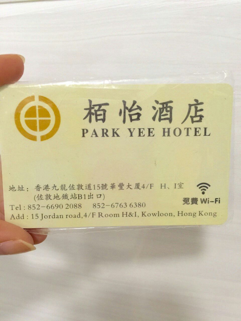 A hotel key card is held in a hand, displaying the name 'Park Yee Hotel' prominently. Contact information and the address are located at the bottom, along with a logo. The background is a plain white surface.