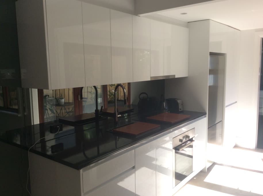 Modern kitchen with oven, cooktop, kettle, toaster, large fridge, microwave... as well as plates, bowls, glasses, cookware etc...