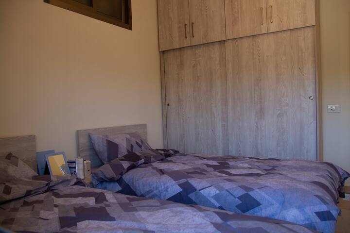 Chumba cha kulala chenye vitanda viwili ikiwemo ukuta kwenye kabati ambalo lina viango na kabati la kuweka vitu 