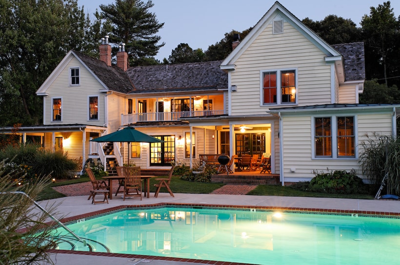 A charming two-story inn is illuminated at dusk, showcasing a serene swimming pool in the foreground. The architectural details feature a mix of windows and porches, while outdoor seating areas are positioned nearby for relaxation.