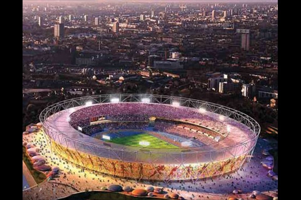 Aerial view of the Olympic Stadium, featuring a circular design surrounded by vibrant seating. The field is illuminated under stadium lights, with crowds visible around the exterior. The cityscape of London is seen in the background, showcasing a blend of buildings and urban life.