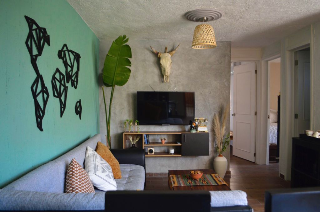 A welcoming living area is highlighted by a stylish sectional sofa in shades of grey and patterned cushions. A wooden coffee table rests on the floor, complemented by an abstract wall art piece. A mounted TV is centered above a sleek storage unit, with decorative plants adding a vibrant touch.