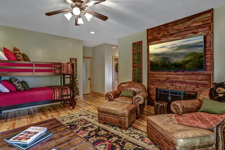 غرفة نوم في الطابق السفلي مع أريكة بسرير بحجم كبير وأسرّة بطابقين وتلفزيون ذكي مقاس 65بوصة