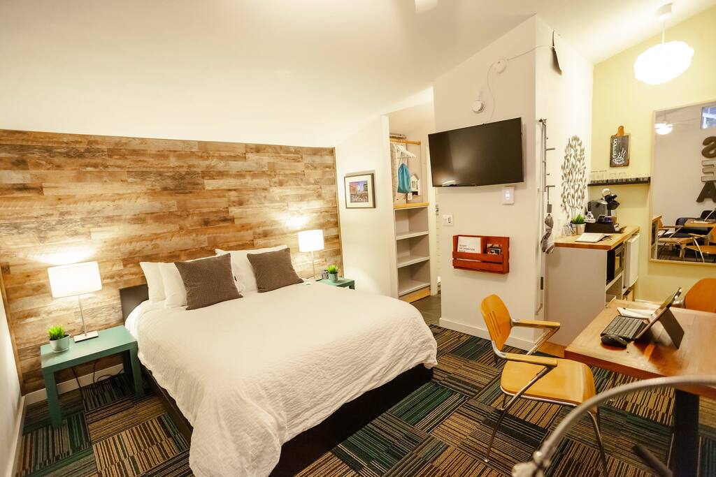 Overview picture of the studio showing the queen sized bed, the coffee bar area and table on the right, TV and Amazon Alexa and finally, the closet in the bathroom.