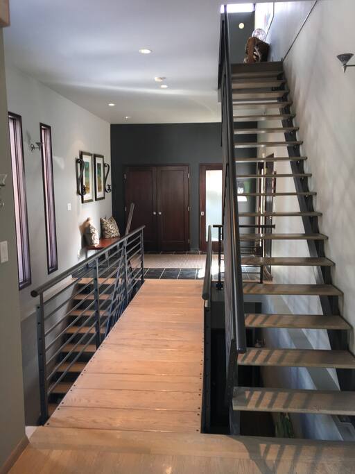 This unique bridge design connects the front entrance to the main floor kitchen and living room areas. The custom floating staircases with hardwood treads and metal railings create a visually dramatic statement.