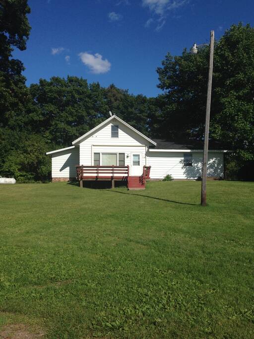 Front view of home with fire pit, grill on deck with table and chairs.