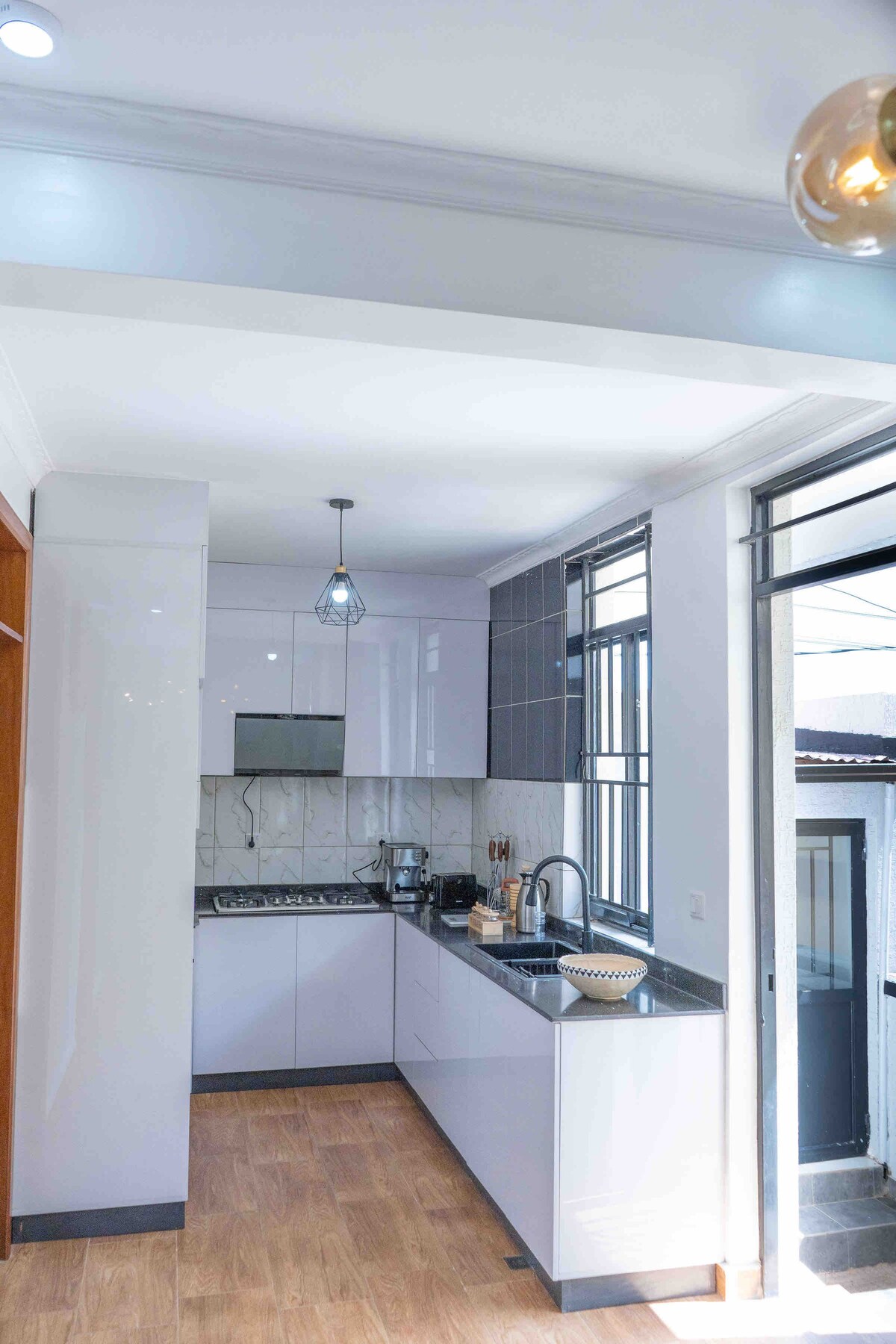 A modern kitchen is depicted, featuring sleek cabinets and a glossy countertop. Natural light filters through multiple windows, illuminating the area. Essential appliances, including a stove and sink, are arranged for convenience. The neutral color palette creates a clean and functional atmosphere.