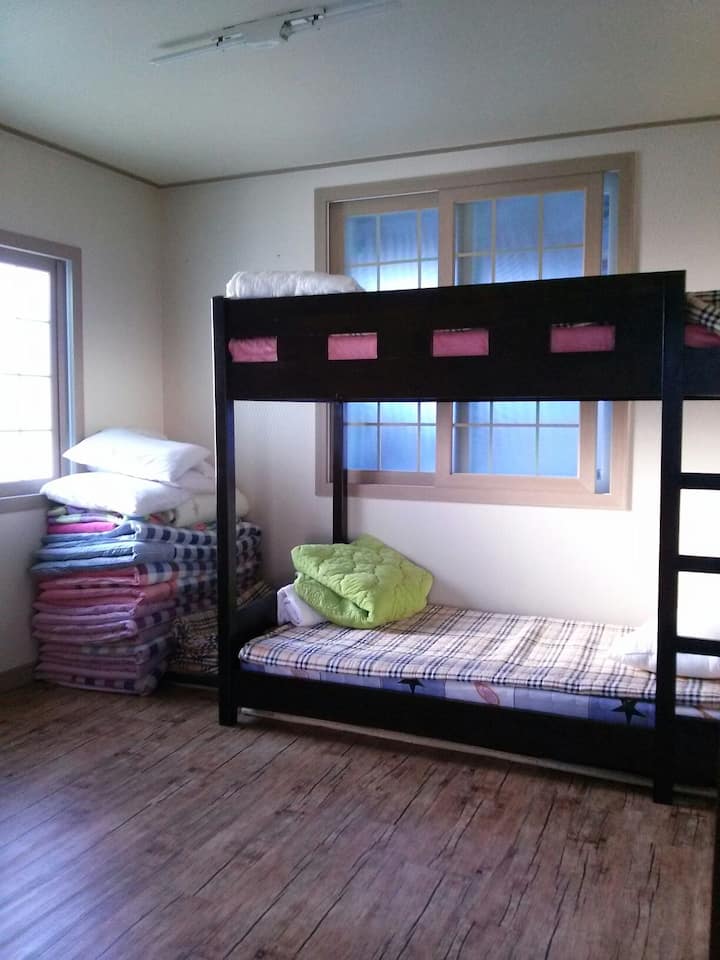 Kuna kitanda cha ghorofa, kiango na meza ya watu wawili katika chumba kidogo.