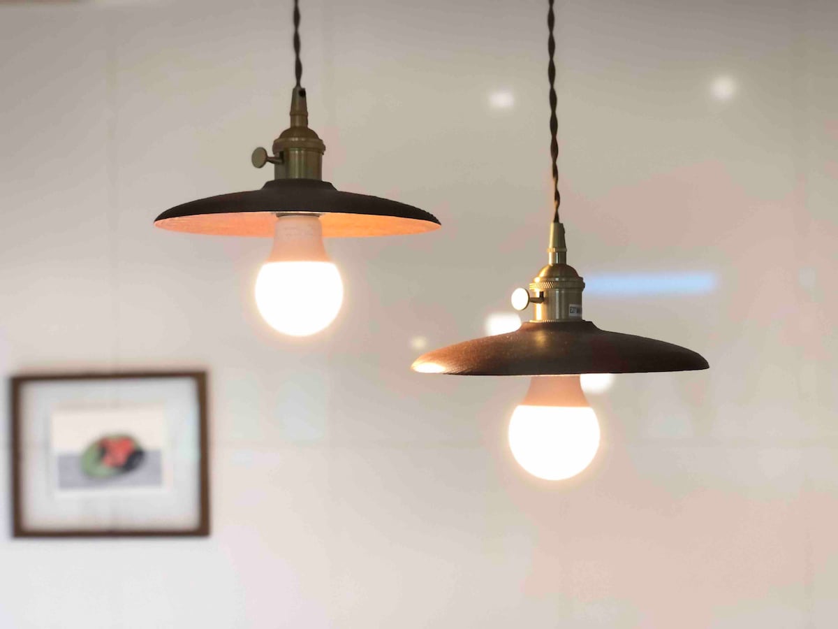 Two pendant lights with metal shades hang from the ceiling, illuminating the space above. One light is turned on, casting a warm glow, while the other is off, showcasing its design. A framed picture can be seen partially in the background.