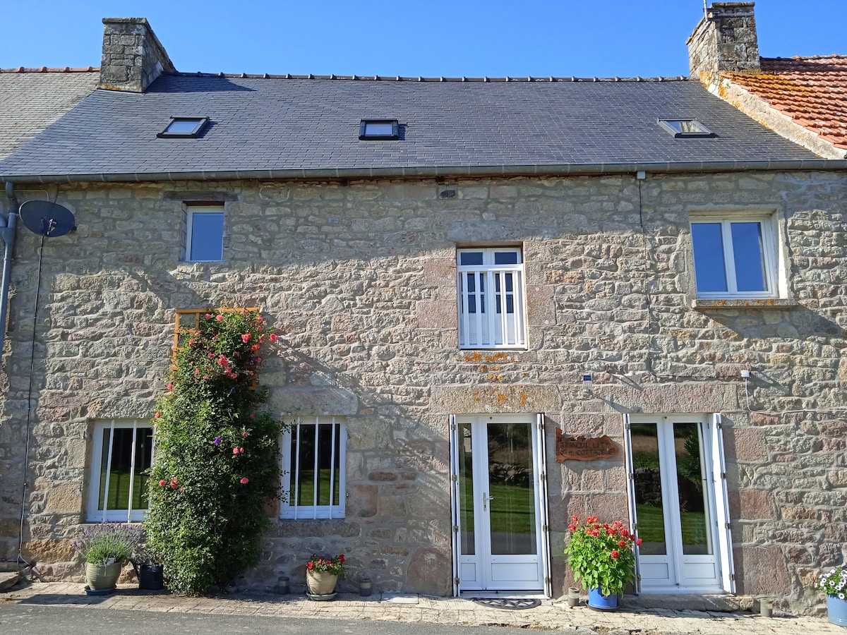 The stone façade of the country house offers a rustic charm, complemented by a neatly trimmed garden with blooming flowers. Large windows allow natural light to brighten the interior. The welcoming entrance is framed by lush greenery, inviting guests into a peaceful retreat.
