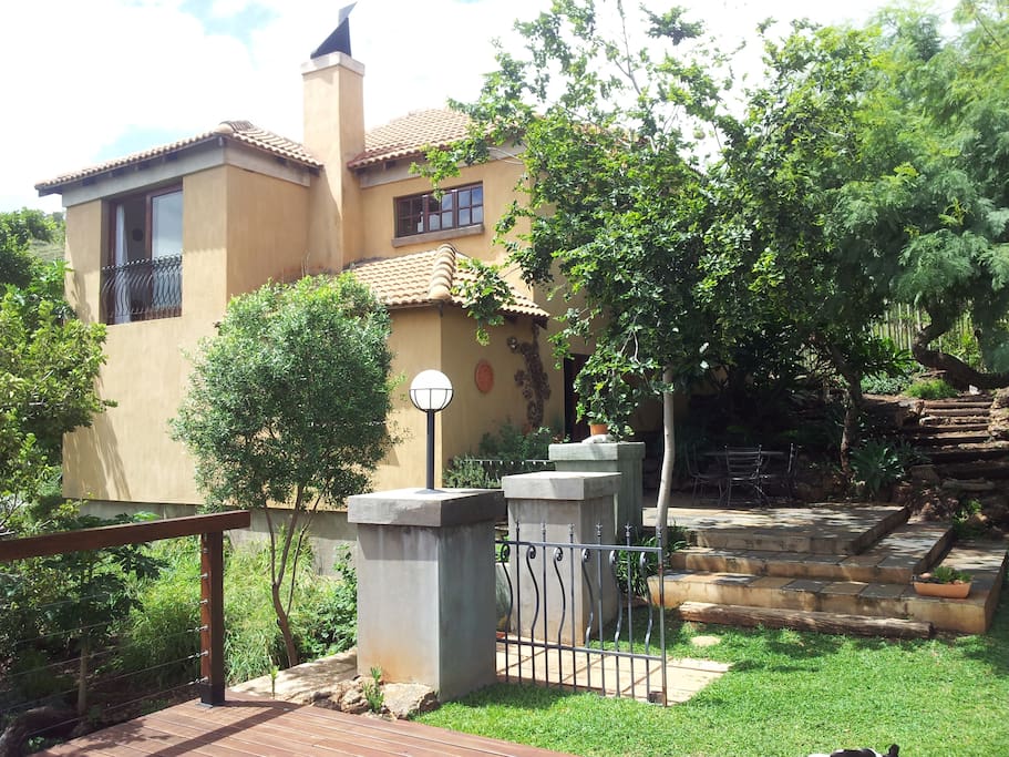 North facing house is nestled in rock. Shady indigenous trees and lawn in front.
